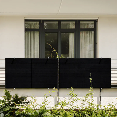 Balkonkraftwerk mit vier schwarzen Solarmodulen am Balkongeländer eines Wohnhauses