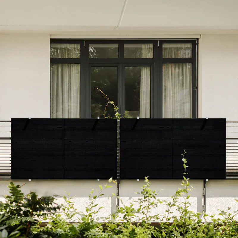 Balkonkraftwerk mit vier schwarzen Solarmodulen am Balkongeländer eines Wohnhauses